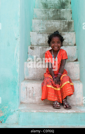 Smiling happy Indian village girl wearing orange dress sitting on some steps.  Andhra Pradesh, India Stock Photo