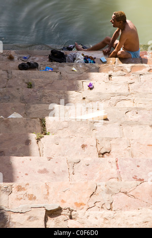 Indian man washing clothes by sitting on the stairs of the water tank. Stock Photo