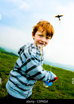 Small boy on a hill top in South Wales UK running in the wind and flying a kite Stock Photo