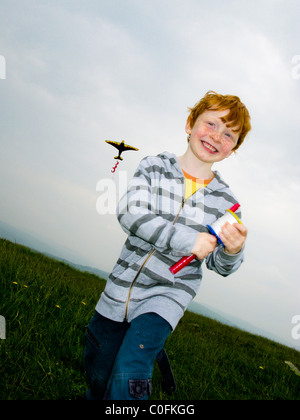 Small boy on a hill top in South Wales UK running in the wind and flying a kite Stock Photo
