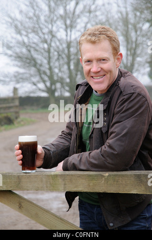 Holding a glass of beer, Adam Henson farmer and television presenter at home on his Gloucestershire farm in the Cotswolds, England Stock Photo