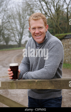 Holding a glass of beer Adam Henson farmer and television presenter at home on his Gloucestershire farm in the Cotswolds England Stock Photo