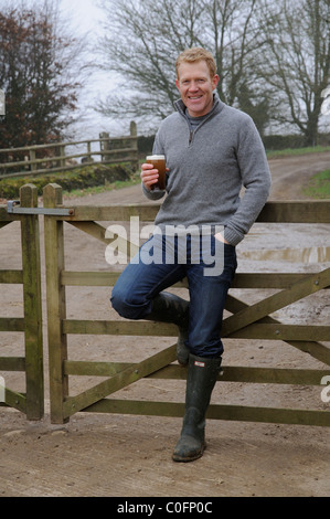 Holding a glass of beer Adam Henson farmer and television presenter at home on his Gloucestershire farm in the Cotswolds England Stock Photo