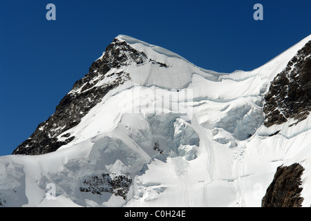 Sheer whiteness of the ice on the mountain summit near the Swiss resort of Jungfrau. The rocky part of the mountain visible. Stock Photo