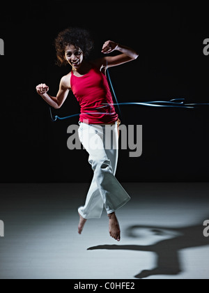 young adult latin american female jumping and playing with led lights doing streaks on black background. Stock Photo