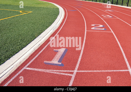 Lanes of a red race track with numbers and green football field Stock Photo