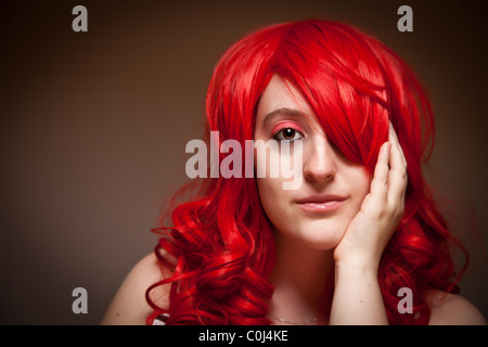 Portrait of Sultry Red Haired Woman with Her Hand on Her Face on a Grey Background. Stock Photo