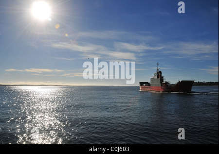 Blue sky view of a vehicle ferry sailing into the morning sun, glistening on the waters of Chacao Channel, Chiloe Island, Chile Stock Photo