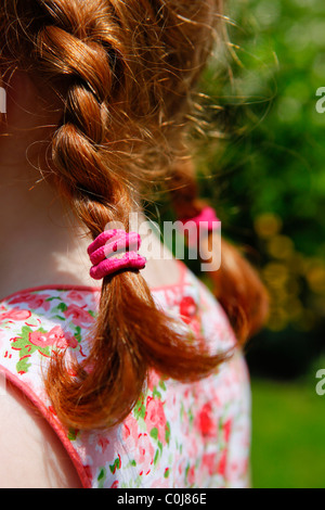 rear view of a little girl with plaits in her garden in the summertime. Stock Photo