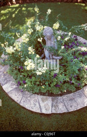 YELLOW AND WHITE SNAPDRAGONS SURROUND 1920'S STATUE IN A SMALL MINNESOTA CIRCULAR GARDEN. SUMMER. Stock Photo