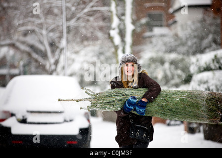 A young woman carrying a Christmas tree along a snowy street Stock Photo