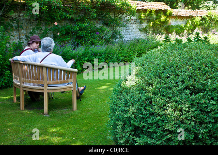 Two elderly women chatting on a wooden bench in an English country garden. Stock Photo