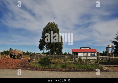 Roadside rural view of red farmhouse with log cart and plastic bucket rain-collection tower, near Ancud, Chiloe Island, Chile Stock Photo