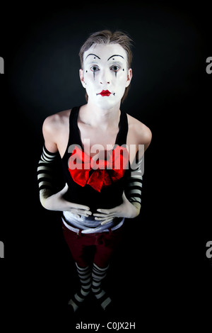Studio portrait of theatrical funny clown with a big red bow on the chest on a black background Stock Photo