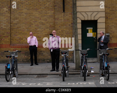 Smoking outside of the office, smokers outside workplace UK in front of row of Barclays rental Boris bikes Stock Photo