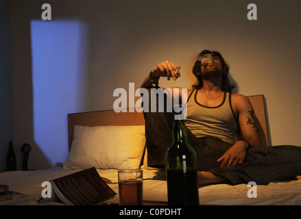 Man smoking on the bed with wine Stock Photo