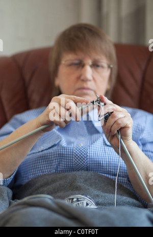 Elder woman doing knitting at home, focus on hands and needles Stock Photo