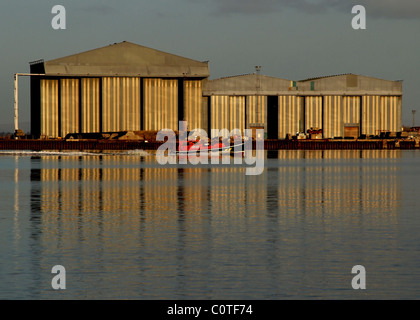 A pilot boat passes the Nigg fabrication yard, reflected in the Cromarty Firth, Scotland. Stock Photo