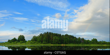 Rainbow and white clouds over  the lake coast. Evening sky. Stock Photo
