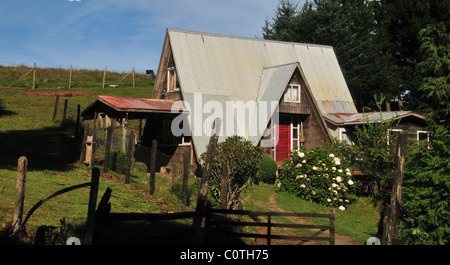 Rural roadside view of a Chilean-German house with high pitched metal roof and wood shingle walls, Caulin, Chiloe island, Chile Stock Photo