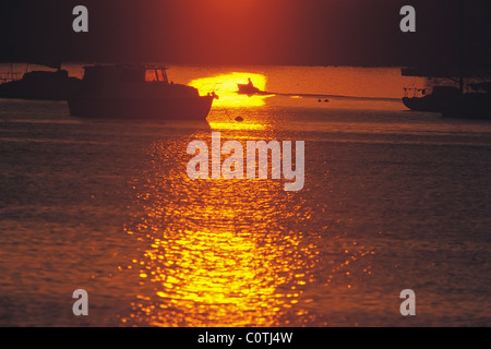 Solitary figure in dinghy silhouetted by sunrise Stock Photo