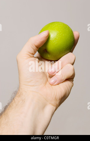 Green apple held by hand isolated on a gray/white/neutral background with space for text or cutout. Stock Photo
