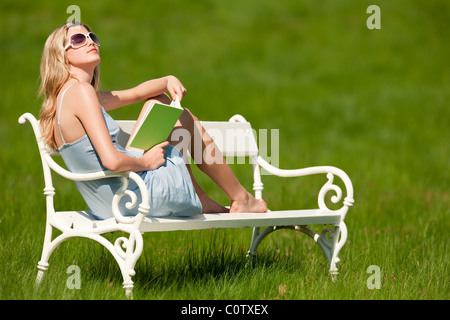 Spring and summer - Young woman relaxing in meadow on white bench on sunny day enjoying sun Stock Photo