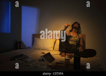 Man smoking on the bed with wine Stock Photo