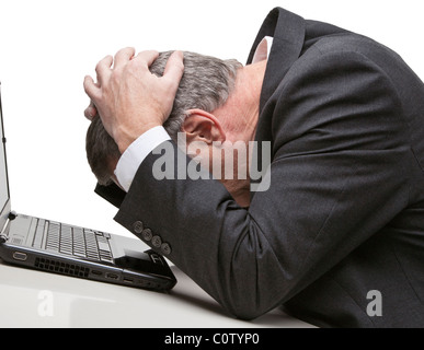 Businessman holding head in hands in front of computer isolated against a white background Stock Photo