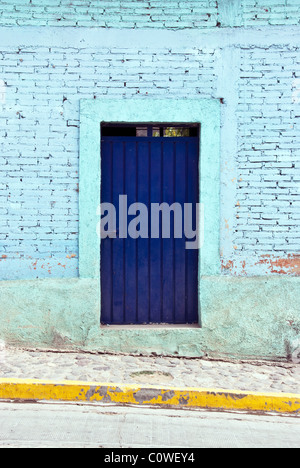cerulean blue painted brick wall with deep blue door stone sidewalk & bright yellow curb marking Teotitlan Oaxaca State Mexico Stock Photo