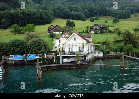 A house, pier and boats, on the shore of Lake Lucerne in Switzerland. The house is located on a green slope, with other houses. Stock Photo