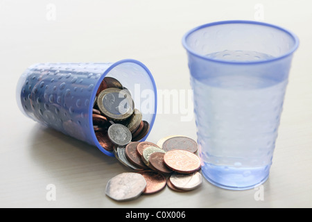 An upturned plastic cup of sterling coins next to a small pile of ...