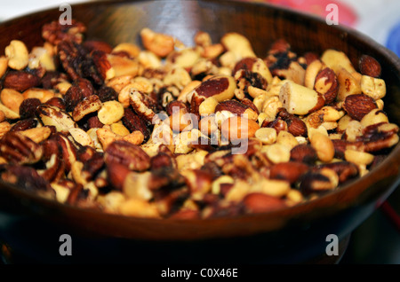 A wooden bowl filled with roasted, salted mixed nuts. Closeup. Stock Photo