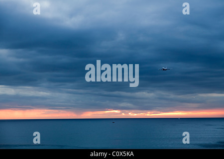 Aircraft passenger jet landing over ocean against cloudy dramatic sky. Dockweiler Beach in Los Angeles, California. LAX.
