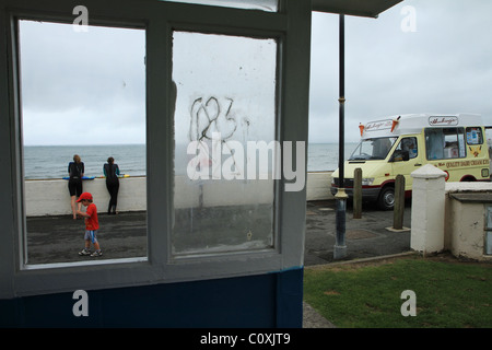 Young boy in red t-shirt walks past seafront shelter, Westward HO!, Devon, UK Stock Photo