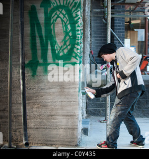 a young man teenager boy youth kid spraying graffiti on a wall, UK Stock Photo