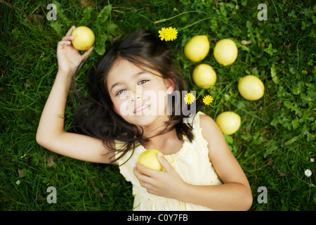 Six year old girl lies on grass lawn with yellow lemons Stock Photo