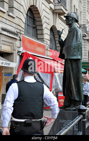 Beat policeman back view patrolling tourist area outside Baker Street Station with Sherlock Holmes sculpture obscured shop sign London England UK Stock Photo