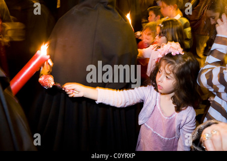 Church member penitent processing in Semana Santa Easter Holy week procession gives candle wax to child / girl, in Seville Spain Stock Photo