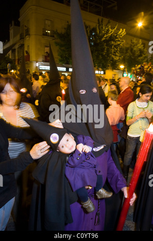 Member of Catholic church, & baby, taking part / processing in Seville's Semana Santa Easter Holy week procession. Seville Spain Stock Photo