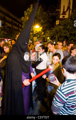 Church member penitent processing in Semana Santa Easter Holy week procession gives candle wax to child / children Seville Spain Stock Photo