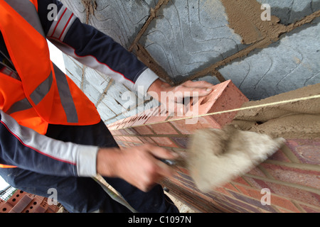 Brick layer with high visibilty jacket laying bricks with a trowel and cement Stock Photo