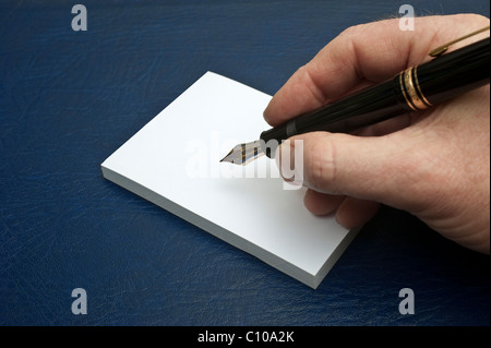 A male hand holding a Mont Blanc Meisterstuck 149 fountain pen about to write on a white writing pad Stock Photo