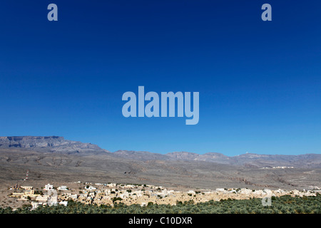 The red, earth colored houses of the Omani village of Al Hamra in the Hajar Mountains, under an azure sky. Stock Photo