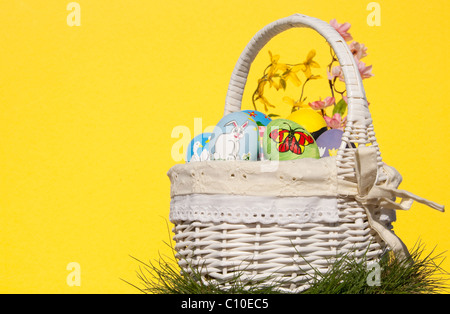 Wicker basket full of colorful hand painted Easter eggs against yellow background Stock Photo