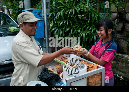 Indonesian primary school children buying after school treats from a street vendor outside their school in Ubud, Bali, Indonesia Stock Photo