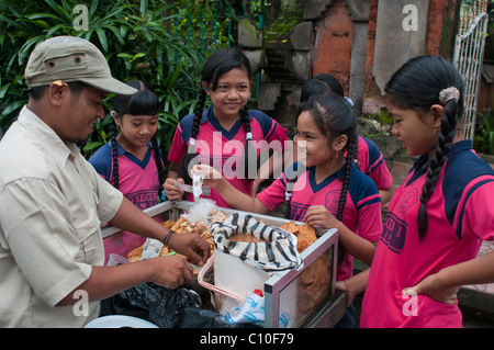 Indonesian primary school children buying after school treats from a street vendor outside their school in Ubud Stock Photo