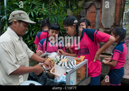 Indonesian primary school children buying after school treats from a street vendor outside their school in Ubud, Bali, Indonesia Stock Photo