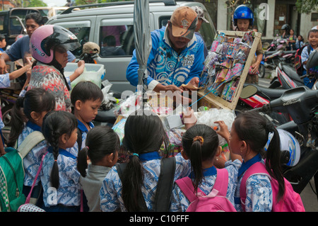 Indonesian primary school children buying after school treats from a street vendor outside their school in Ubud, Bali, Indonesia Stock Photo