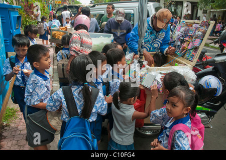 Indonesian primary school children buying after school treats from a street vendor outside their school in Ubud, Bali, Indonesia Stock Photo